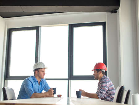 two handsome engineers are gossiping at workplace with panorama windowの写真素材