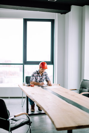 young foreman is making up a model of new skyscraper in the office room with modern interior