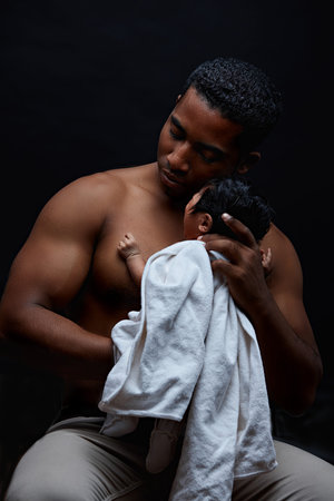 brutal strong afro man sitting with his newborn child. close up portrait. isolated on the black...