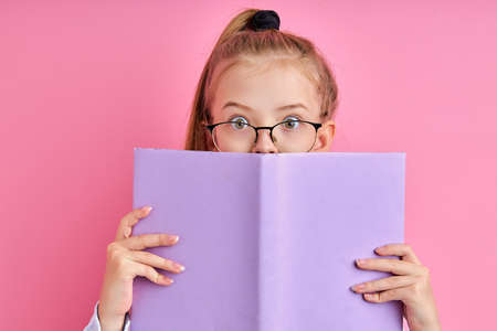adorable caucasian girl in eyeglasses read a book isolated, smart intelligent child love learning, studying, keen on educationの写真素材