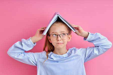 wonk child girl with book on head isolated, little caucasian child in eyeglasses looking away, read...