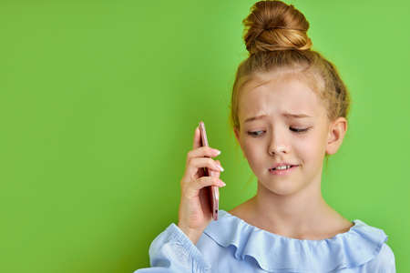 little girl misunderstands the talk on phone, she emotionally reacts on talk, hold smartphone next to eatの写真素材