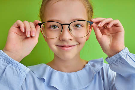 adorable caucasian kid girl looking at camera through eyeglasses, beautiful girl gazing and smiling, isolated over green backgroundの写真素材