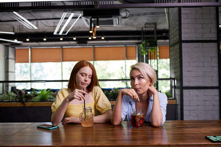 two caucasian ladies are bored of spending time at the bar, sit depressed and unhappy, want to go outの写真素材