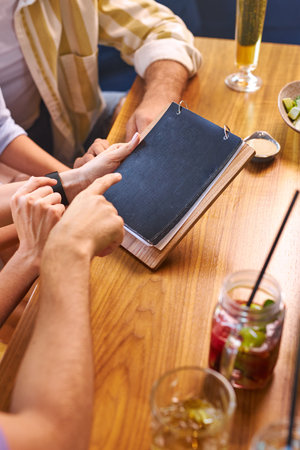 leisure, people and holidays concept. group of friends reading menu at restaurant, choose and going...