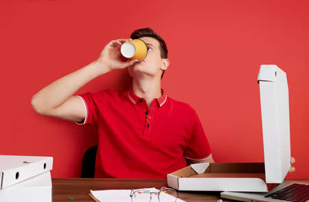good-looking male drink coffee at work place, sits in the office. isolated red backgroundの写真素材