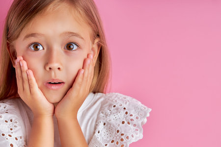 portrait of little caucasian girl in shock, she is surprised by something, hold hands on cheek,...