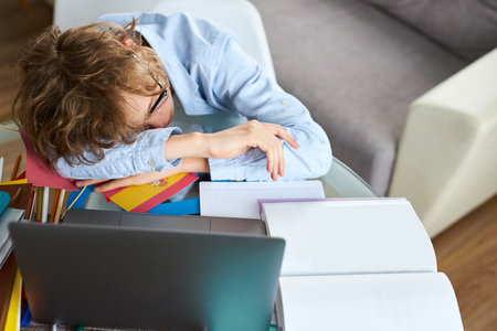 young schoolboy sleep while doing homework online, tired to study, at home in bedroom