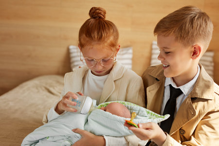 children want to be parents for child, redhead girl and boy sit on bed at home holding baby in hands, love conceptの写真素材