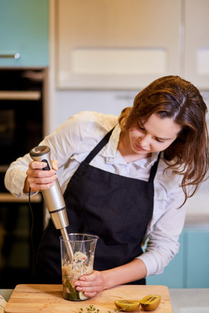 young attractive woman holding a blender and looking at the jar, close up photo. preparation of...