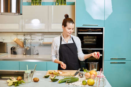 young pleasant woman is holding slices of apples in hands and looking at the table. copy space.の写真素材