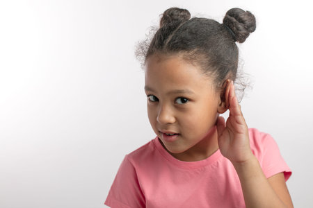 beautiful girl with dark hair in pink fashon dress is listening with her hand on an ear.copy space....