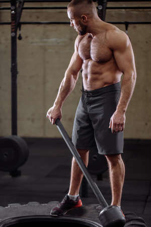 back view photo. man of muscle is gripping the sledgehammer in the roomの写真素材