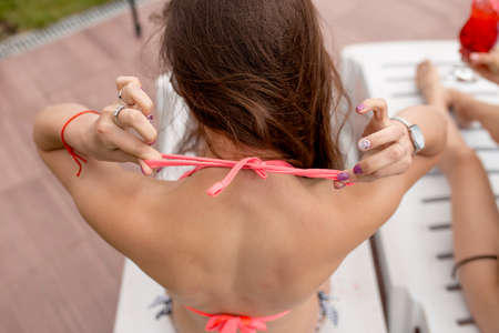 Slim girl putting on a separate bright pink swimsuit.back view photo. woman is tying her swimsuit before swimming. close up photo.の写真素材