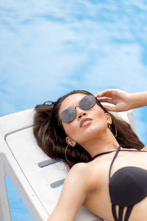 sweet girl with perfect appearance with beautiful makeup resting on the lounge by the hotel pool. close up cropped photo.の写真素材
