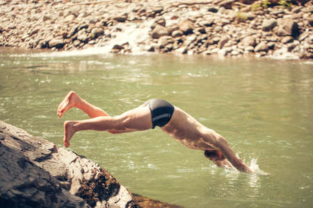 One man jumping into a forest lake on a summer day. Summer Vacation and Tourist Activities.の写真素材