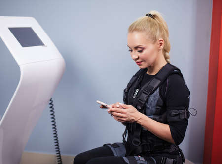 close up side view photo of a cheerful blond female holding her smart phone while working out in the sport club. free time, hobby conceptの写真素材