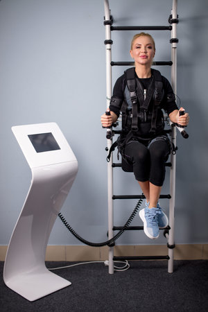 fit beautiful female working out in ems suit on parallel bars in the fitness club, sport and health conceptの写真素材