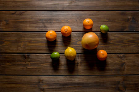 Whole ripe fresh citrus fruits, such as grapefruits, limes, lemons, oranges and mandarins in the middle on brown wooden table. Top view, copy space.の写真素材