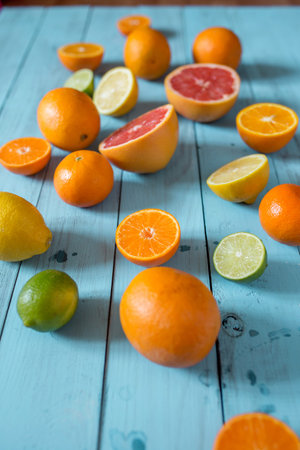 Tropical citrus fruits, whole and sliced oranges and lemons of different colours on blue wooden...