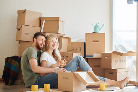 married couple sitting near cardboard boxes in new apartment relaxing after unpacking boxes