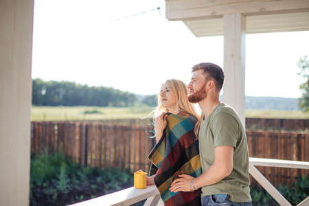 modern new house with terrace, couple standing and drink coffee with plaid relaxing enjoying beautiful viewの写真素材