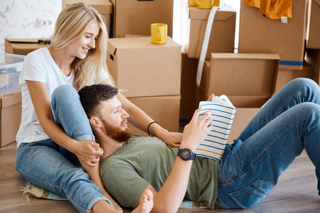 Couple sitting on floor reading book with boxes in the living room. Moving house couple relax...