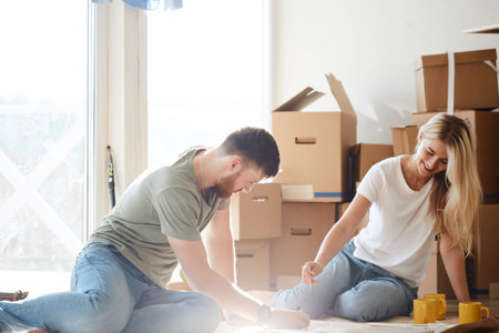 Young couple sitting at floor moving into new home looking at floor plans together