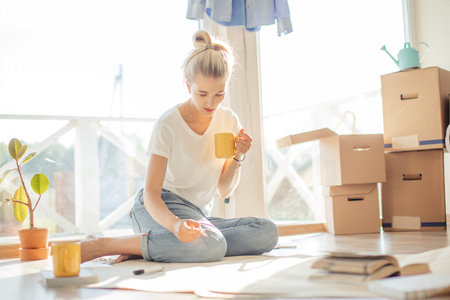 Portrait of smiling woman sitting on floor of new house making plan to furniture their home on paper