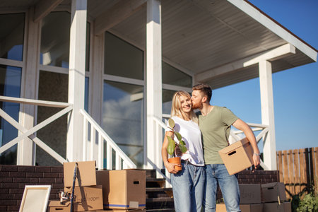 Young happy couple huging and kiss outside with moving boxes at new home