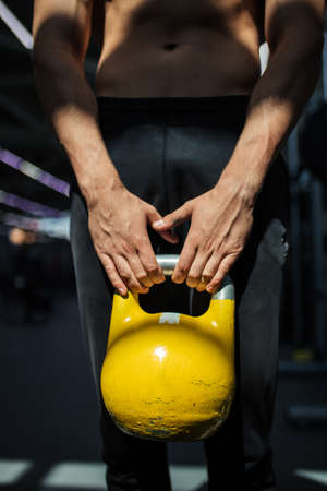 Young muscular man working out with yellow kettlebells. Photo of man with naked torso training in modern gym. Strength and motivationの写真素材