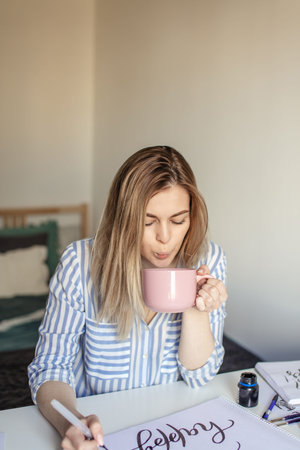Close up photo of woman writing beautiful notes on paper on white desk while drink coffee or tea