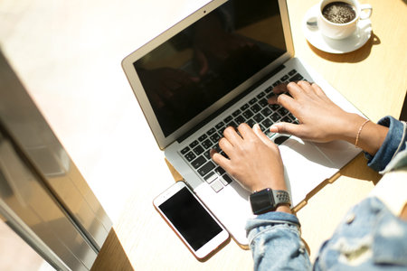 High angle view of African female blogger, typing a new post during lunchtime at a cafe, working...