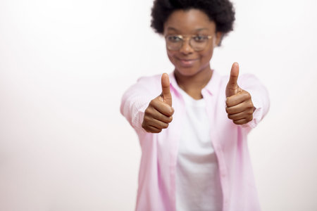 focus on two thumbs up. happy afro female shows encouragement. females face on the blurred...