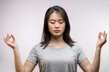 Young Asian woman with closed eyes spreading hands with mudra gestures, seeking for peace in mind. Mind Balance condition, Isolated studio shot with copy space.の写真素材