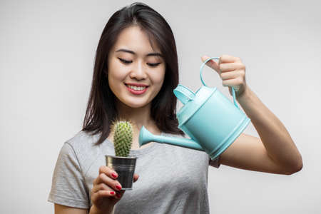 Asian attractive happy female model watering little green cactus in flowerpot by small blue watering can, symbolizing dry skin or hair need water, Moisturizing Skin and Hair Ritual Concetの写真素材