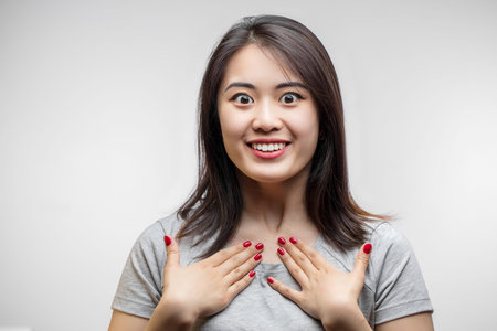 Asian cheerful young woman, wearing loose white T-shirt, posing against white blank wall. Happy...