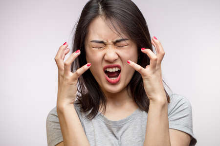 Furious frustrated Asian woman yells loudly, screws up her eyes, gesturing with hands desperately, isolated over white background with copyspace, Negative Emotions and Gesturesの写真素材