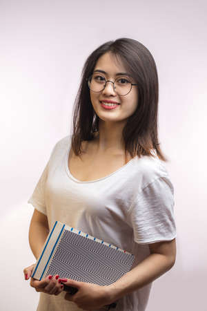 Asian smiling student girl with books, dressed casually, looking with satisfaction at camera, being happy. Studio shot of good-looking appealing Korean woman isolated against blank studio wall.の写真素材