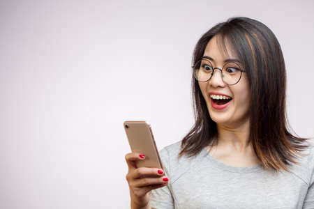 Overjoyed Asian woman in spectacles laughing , reading funny story in social media, browsing internet on smartphone.の写真素材