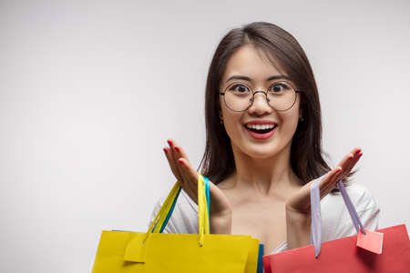 Shopping becomes pleasure if you have unlimited credit card. Happy Asian woman enjoying shopping, holding colorful shopping bags in both hands and looking at camera with overjoyed expression.の写真素材