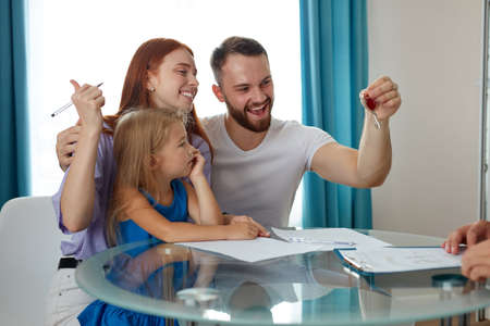 happy male with wife and daughter get keys from their first house, they sit excited, sign the documents to get mortgageの写真素材