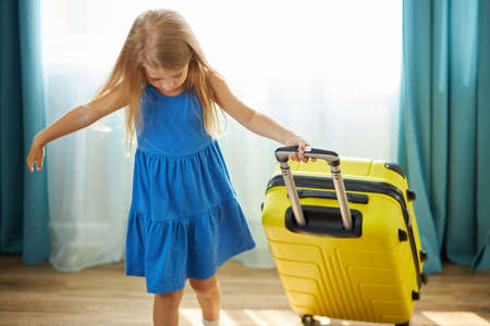 happy little caucasian child girl tourist packs clothes into a yellow suitcase for travel, vacation. alone in living roomの写真素材