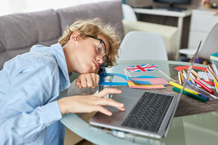 sleepy exhausted teen boy want to sleep, he is tired to study. he sits at table with laptop, doesnt want to learn lessonsの写真素材