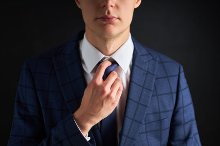 serious confident guy in executive suit fix a tie isolated over black background. trendy rich guy posing at cameraの写真素材