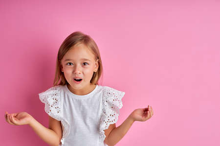 portrait of surprised little girl spread her arms, in shock, isolated pink backgroundの写真素材