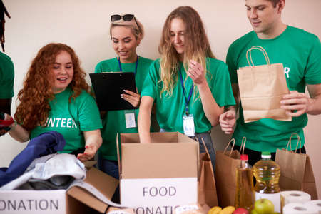 happy young volunteers donating clothes and food for charity, indoors. active ethusiastic volunteering team putting stuff into boxes for poor people. kindness and generosity conceptの写真素材