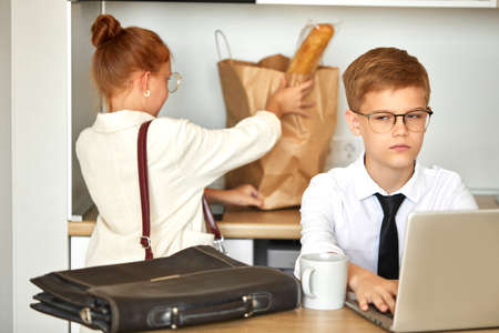 little caucasian boy work on laptop at home, young office worker in formal wear is concentrated on online work, during quarantine. children pretend to be adultsの写真素材