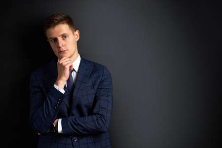 portrait of caucasian handsome male in stylish suit posing at camera, isolated over black background. business people concept. in contemplationの写真素材