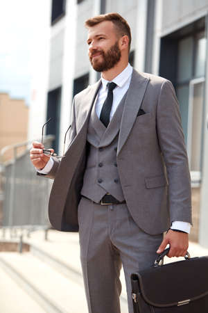 portrait of handsome caucasian businessman with bag going at business meeting, in formal suit outdoorsの写真素材